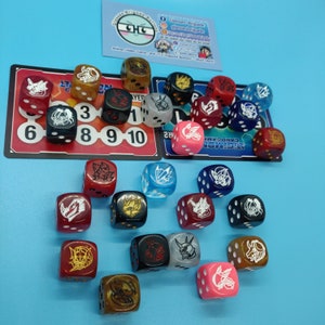 Peut inclure: Un ensemble de 18 dés colorés avec différents motifs, dont un logo de jeu de cartes Digimon, sont éparpillés sur une surface bleue. Les dés sont rouges, bleus, verts, jaunes et blancs.