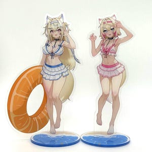 Op de afbeelding: Twee anime-achtige figuren van vrouwen in badpakken. Eén figuur houdt een oranje opblaasbare ring vast. De figuren hebben blond haar, dierenoren en staarten. De badpakken zijn wit en blauw en roze. Ze staan op heldere bases met een blauw oceaanontwerp.