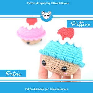 May include: A crochet amigurumi cupcake pattern with a blue and white frosting and a red cherry on top. The cupcake has a brown base and a cute face with black eyes and a pink blush. The pattern is designed by GanchiGurumi.