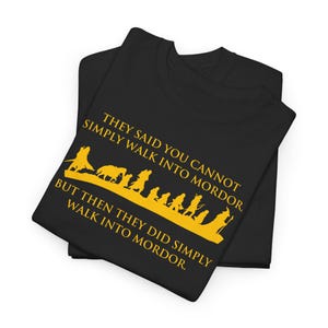 Peut inclure: T-shirts noirs avec un graphisme et du texte jaunes. Le graphisme représente des silhouettes de personnages marchant, avec le texte "THEY SAID YOU CANNOT SIMPLY WALK INTO MORDOR, BUT THEN THEY DID SIMPLY WALK INTO MORDOR."