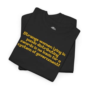 May include: Two black t-shirts, folded and stacked, with yellow text that reads: "Strange women lying in ponds distributing swords is no basis for a system of government!"