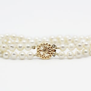 May include: A double strand pearl bracelet with a gold clasp. The clasp is a round, ornate design.