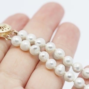 May include: A double strand pearl necklace with a gold clasp. The necklace is made of white pearls and is on a hand.