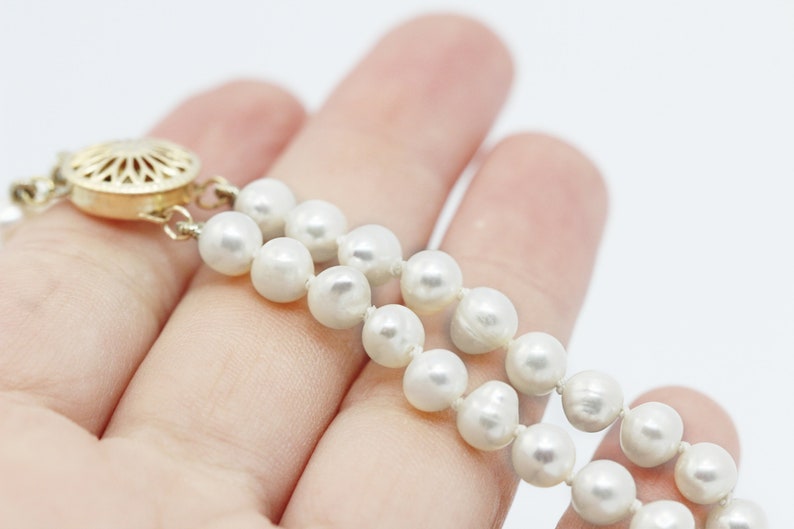 May include: A double strand pearl necklace with a gold clasp. The necklace is made of white pearls and is on a hand.