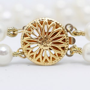May include: A gold-toned clasp with a delicate floral design, connecting two strands of white pearls.