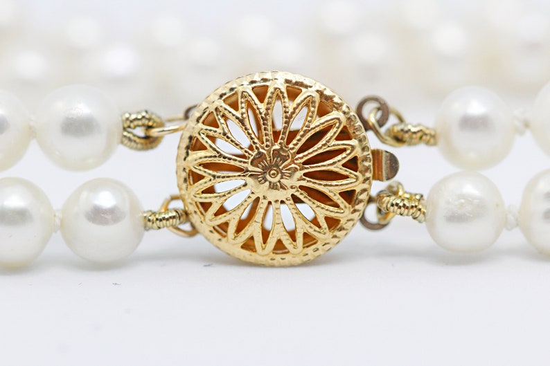 May include: A gold-toned clasp with a delicate floral design, connecting two strands of white pearls.