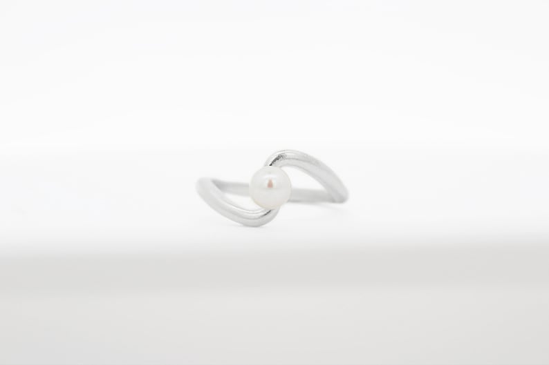 May include: A silver ring with a single white pearl set in a curved band.