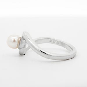 May include: A silver ring with a single white pearl set on the side. The ring has a simple, elegant design.