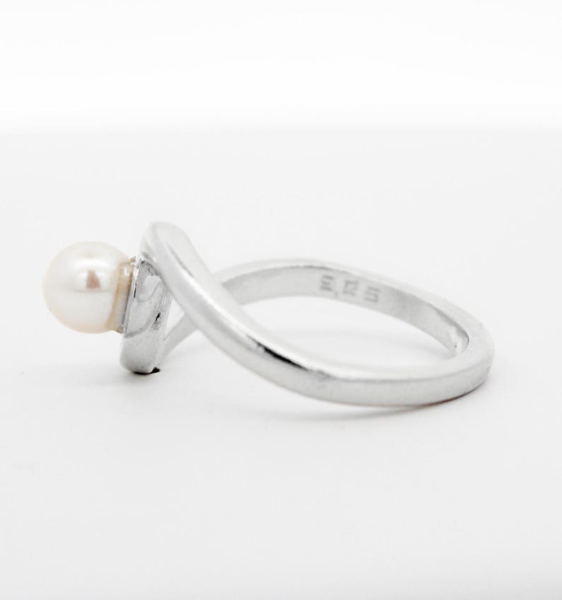 May include: A silver ring with a single white pearl set on the side. The ring has a simple, elegant design.