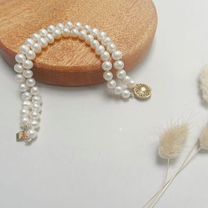 May include: A double strand pearl necklace with a gold pendant featuring a floral design.
