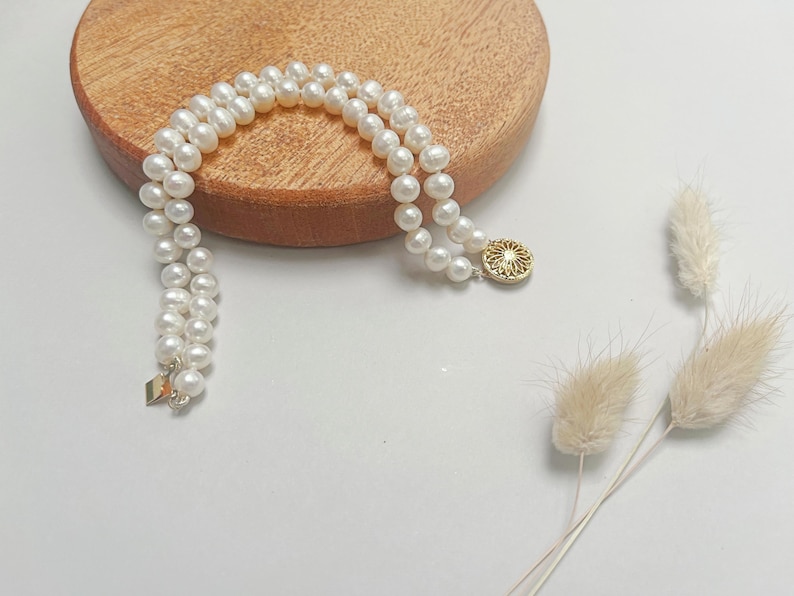 May include: A double strand pearl necklace with a gold pendant featuring a floral design.