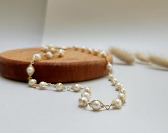 May include: A delicate gold necklace with white pearls, each pearl is wrapped in gold wire. The necklace is on a wooden surface.