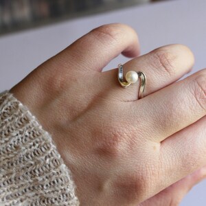 May include: A silver ring with a white pearl set in a curved band.