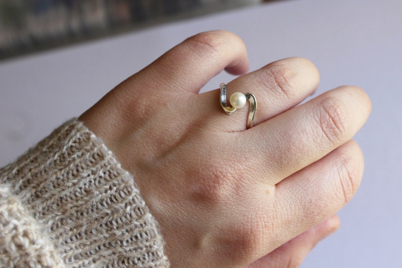 May include: A silver ring with a white pearl set in a curved band.
