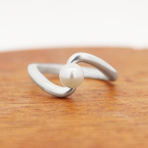 May include: A silver ring with a white pearl set in a curved band.