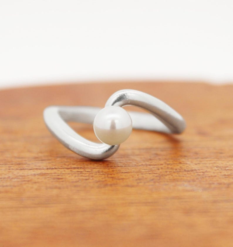 May include: A silver ring with a white pearl set in a curved band.