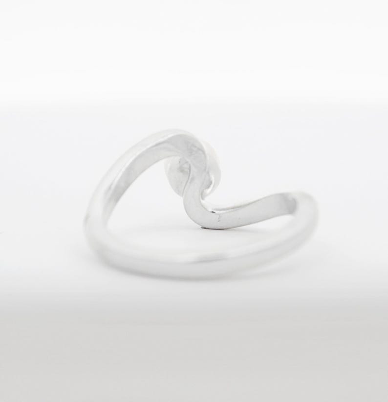 May include: A silver wave ring. The ring is made of a single piece of metal that is bent into the shape of a wave.