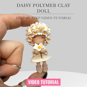 May include: A polymer clay doll with a daisy theme. The doll wears a white dress and a daisy crown, and holds a daisy. The text "DAISY POLYMER CLAY DOLL" and "STEP-BY-STEP VIDEO TUTORIAL" are displayed above the doll. The text "VIDEO TUTORIAL" is displayed below the doll.