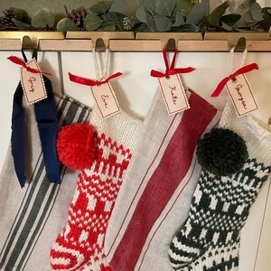 Hand embroidered name tags in red thread with red ribbon, attached to four Christmas stockings