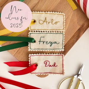 Three name tags with hand embroidered names, in gold, emerald green and dark red for Christmas presents