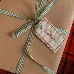 fabric name tag with hand embroidered name ‘Foster’ in red thread, attached to a present with green gingham ribbon