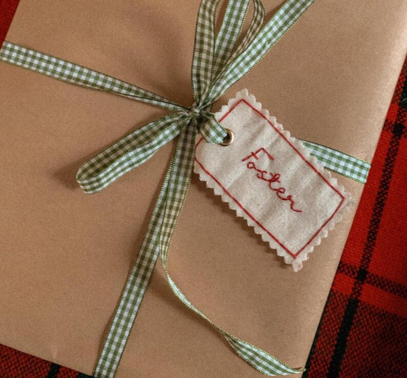 fabric name tag with hand embroidered name ‘Foster’ in red thread, attached to a present with green gingham ribbon