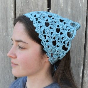 May include: A light blue crocheted bandana with a delicate floral pattern. The bandana is tied around the head of a person with long brown hair.