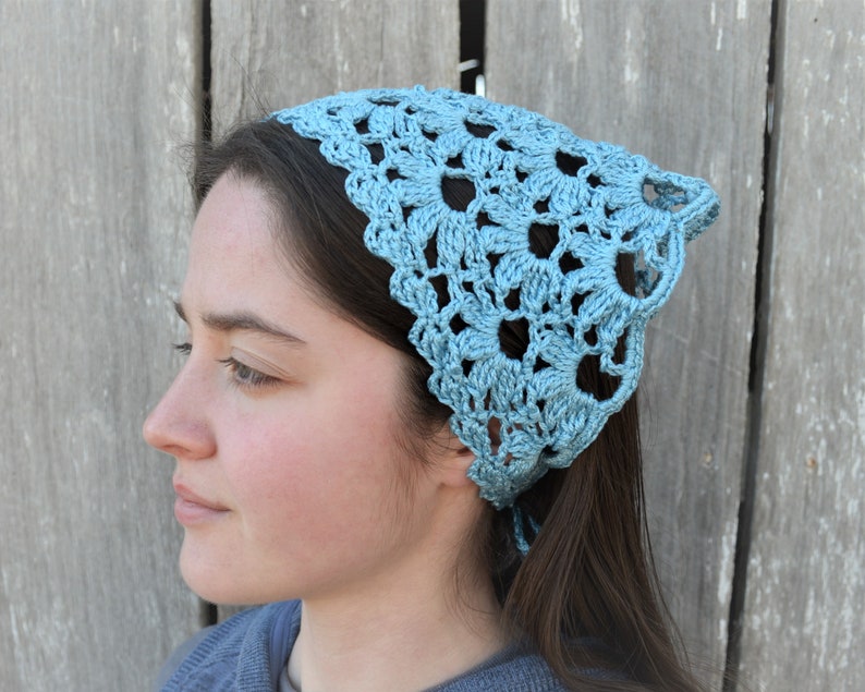 May include: A light blue crocheted bandana with a delicate floral pattern. The bandana is tied around the head of a person with long brown hair.