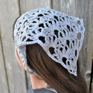May include: A light gray crocheted bandana with a delicate floral pattern. The bandana is tied around the head and hangs down the back.