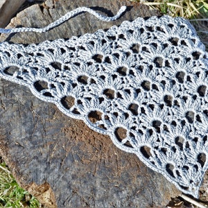 May include: A gray crocheted shawl with a delicate openwork pattern. The shawl is laid out on a rough wooden surface.