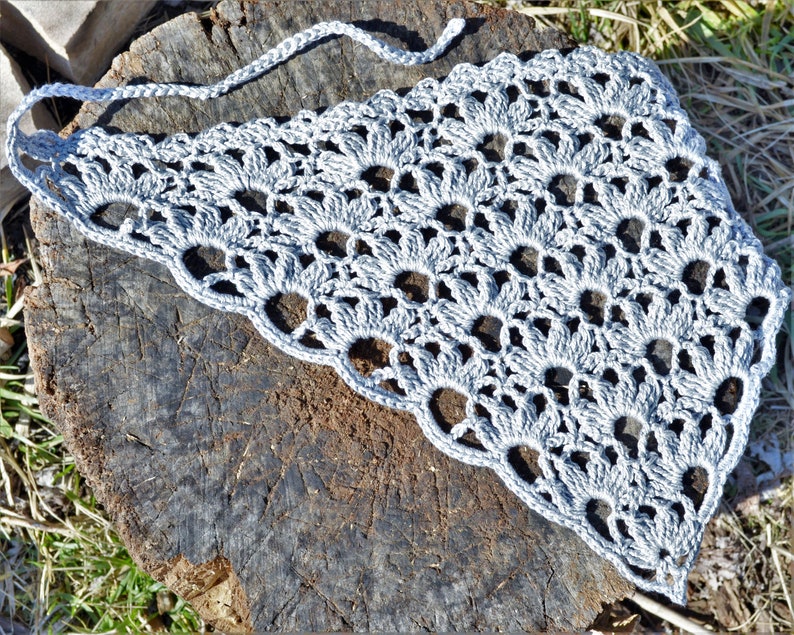 May include: A gray crocheted shawl with a delicate openwork pattern. The shawl is laid out on a rough wooden surface.