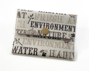 Può includere: Un portafoglio in tessuto beige con una copertura in plastica trasparente. Il portafoglio presenta un design di gufo marrone e le parole "Fresh Air", "Environment", "Nature", "Environment", "Water" e "Habit" stampate su di esso.