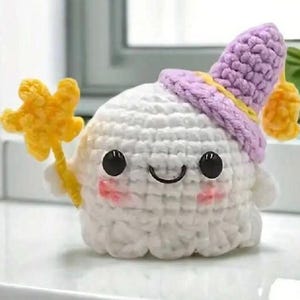 May include: A white crocheted ghost wearing a purple hat with a yellow star. The ghost has black eyes and a smiling mouth.
