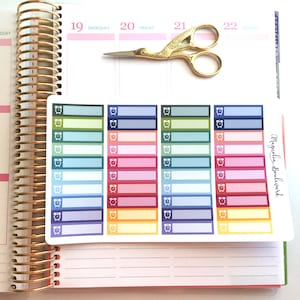 May include: A sheet of colorful planner stickers with alarm clock icons and blank spaces for writing. The stickers are arranged in rows and columns, with each row featuring a different color scheme. The stickers are printed with the text "Magnolia Boulevard".