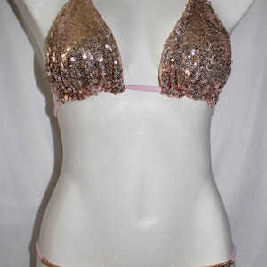 May include: A gold and pink sequined bikini top and bottom. The top is a triangle style with thin pink straps. The bottom is a cheeky style with a low rise.