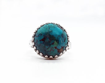 May include: A turquoise ring with a silver setting. The ring has a round stone with a detailed silver border.