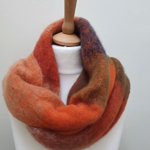 May include: An infinity scarf in autumnal shades of orange, rust, and brown. The soft, textured scarf is displayed on a white mannequin head. The colour gradient creates a warm feel, ideal for colder weather.