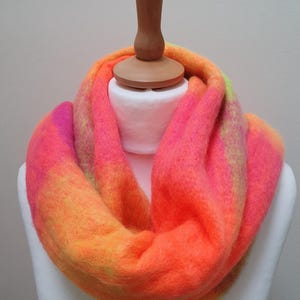 May include: A brightly coloured infinity scarf in shades of pink, orange, and yellow, displayed on a mannequin. The scarf's gradient effect creates a warm, inviting look. The soft, fuzzy texture suggests a cosy winter accessory, perfect for colder weather.