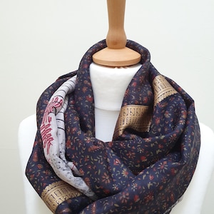 May include: A navy blue infinity scarf with a floral pattern in red and gold. The scarf is displayed on a white mannequin. The scarf has a gold border and a section with a red and white design.