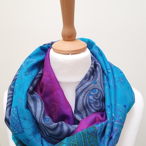 May include: An infinity scarf featuring a vibrant patchwork of blue, turquoise, and magenta fabric panels. The scarf displays a variety of intricate patterns, including paisley, floral, and geometric motifs, layered to create a textured appearance.