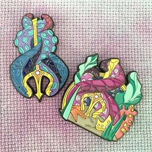 May include: Two enamel pins featuring an octopus with a trident and an octopus with a seashell. The octopus with the trident is blue, purple, and yellow. The octopus with the seashell is pink, purple, and green.