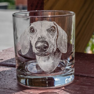 Puede incluir: Un vaso de vidrio transparente con una imagen grabada de un perro salchicha. El perro est&aacute; de frente con las orejas levantadas y la lengua fuera.