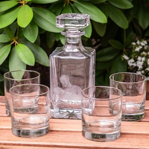 May include: Four clear glass tumblers and a clear glass decanter with a square base and a square stopper. The decanter has an etched design of a person's face.