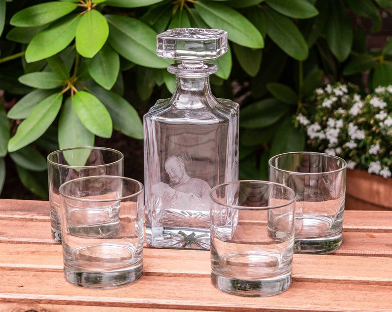 May include: Four clear glass tumblers and a clear glass decanter with a square base and a square stopper. The decanter has an etched design of a person's face.