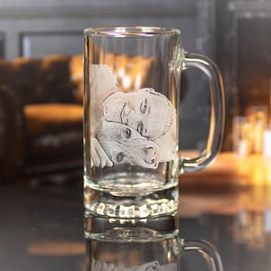 May include: A clear glass beer mug with a handle, featuring an etched image of a person and a dog.