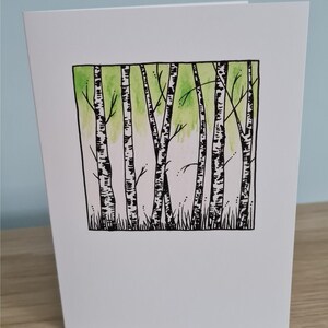 Puede incluir: Una ilustraci&oacute;n en blanco y negro de un bosque de abedules con un lavado de acuarela verde en el fondo.