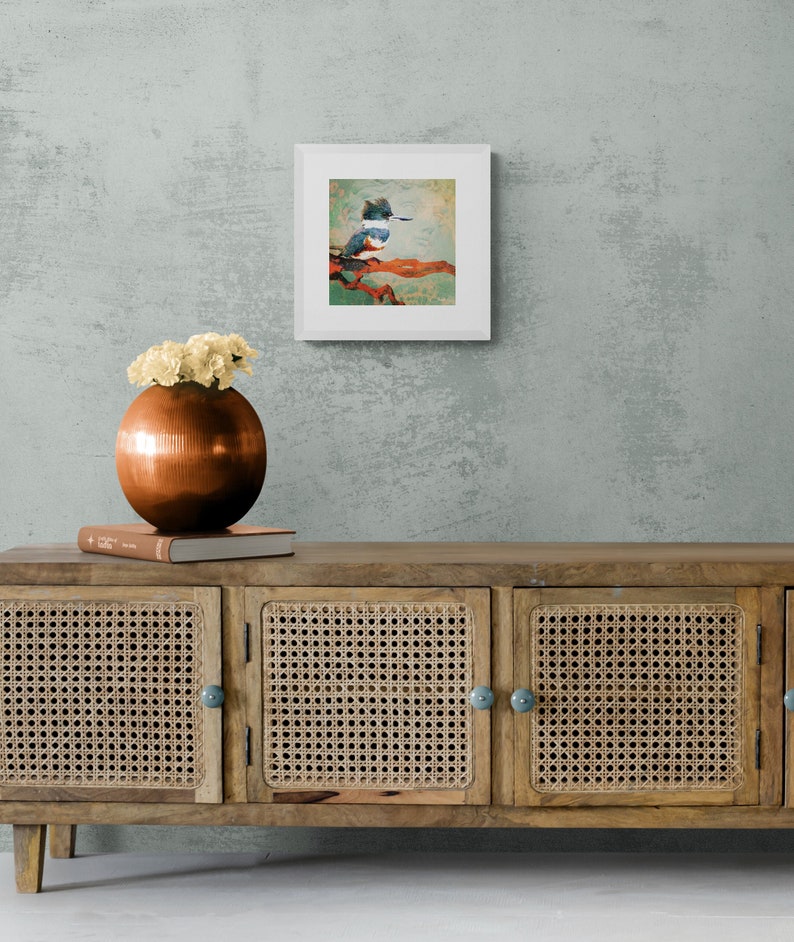 May include: A framed print of a colorful painting of a kingfisher perched on a branch. The painting is set against a light green background. The frame is white and has a simple design.