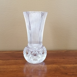 May include: A clear glass bud vase with a textured, ribbed design. The vase has a round base and a narrow opening.