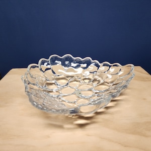 May include: A clear glass bowl with a textured, bubble-like design. The bowl is oval-shaped and has a slightly raised rim.