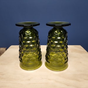 May include: Two olive green glass goblets standing upside down on their rims. Each goblet features a distinct geometric honeycomb pattern across the body, a smooth circular base at the top, and a smooth circular rim at the bottom.